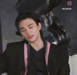 A Young Man Wearing A Black Jacket And A Pink Strap Around His Neck Is Taking A Picture With A Camera . GIF