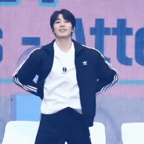 A Young Man Wearing A Black Jacket And A White Shirt Is Standing On A Stage . GIF