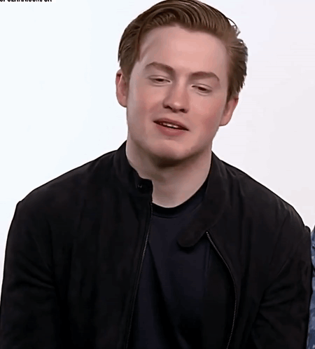 A Young Man Wearing A Black Jacket And Black Shirt Looks At The Camera GIF
