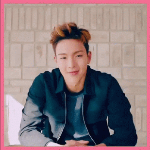 A Young Man Wearing A Black Jacket Is Sitting In Front Of A Brick Wall . GIF