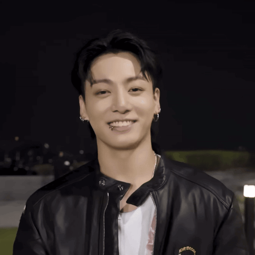 a young man wearing a black leather jacket and earrings smiles