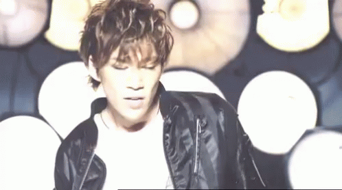 A Young Man Wearing A Black Leather Jacket Is Standing In Front Of A Wall Of Lights . GIF