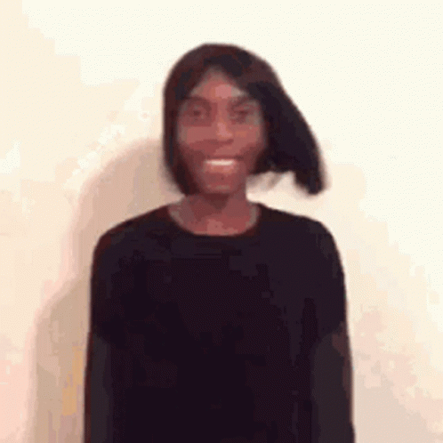 A Young Man Wearing A Black Shirt And A Wig Is Smiling . GIF