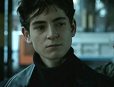 A Young Man Wearing A Black Turtleneck And A Black Leather Jacket Looks At The Camera GIF