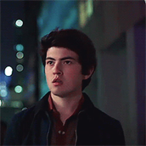 A Young Man Wearing A Blue Jacket And A Brown Shirt Looks At The Camera GIF
