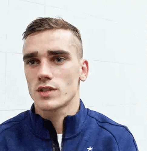 A Young Man Wearing A Blue Jacket With A Star On It Is Standing In Front Of A White Wall . GIF