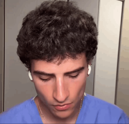A Young Man Wearing A Blue Scrub And White Earbuds GIF