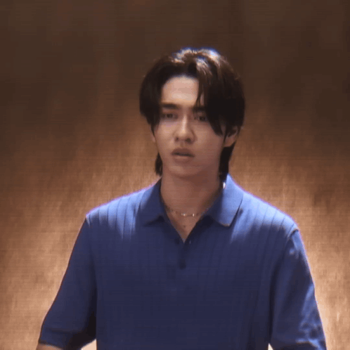 A Young Man Wearing A Blue Shirt And A Necklace Is Looking At The Camera GIF