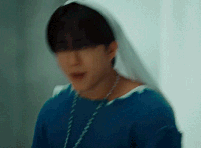 A Young Man Wearing A Blue Shirt And A White Veil Is Standing In Front Of A Window . GIF