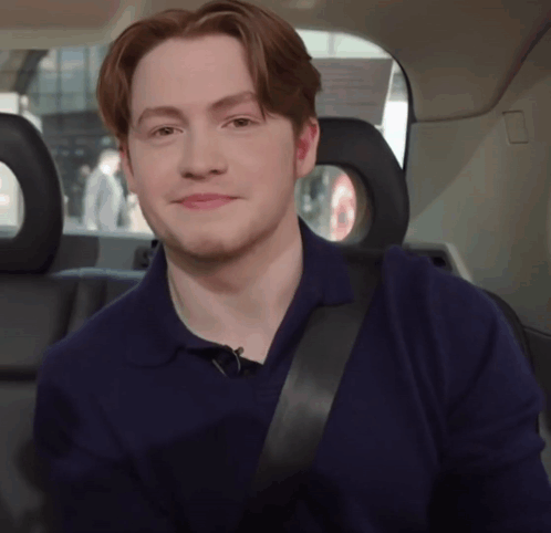 A Young Man Wearing A Blue Shirt And Black Seat Belt Smiles GIF