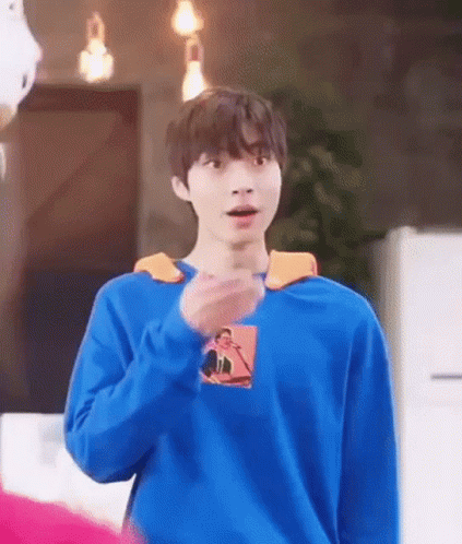 A Young Man Wearing A Blue Sweater Is Standing In A Room . GIF