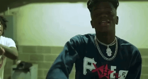 A Young Man Wearing A Blue Sweatshirt And A Necklace Is Standing In A Room . GIF