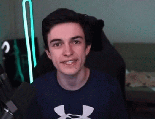 A Young Man Wearing A Blue Under Armour Shirt Is Sitting In A Chair And Smiling . GIF