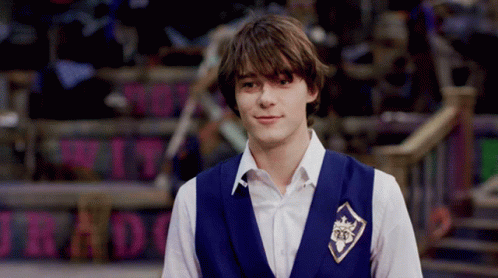 A Young Man Wearing A Blue Vest With A Badge That Says 25 On It GIF