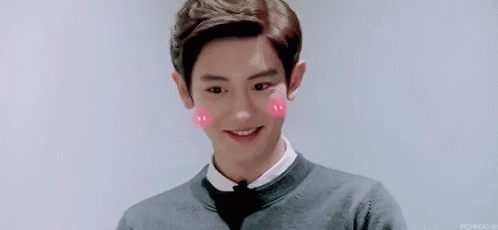 A Young Man Wearing A Bow Tie And A Sweater Is Smiling With Pink Hearts On His Cheeks . GIF