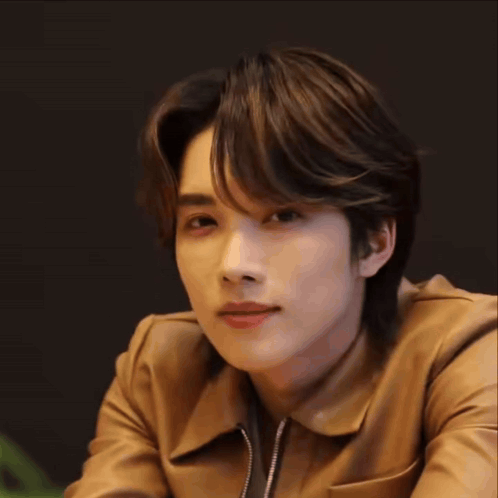 a young man wearing a brown leather jacket is smiling .