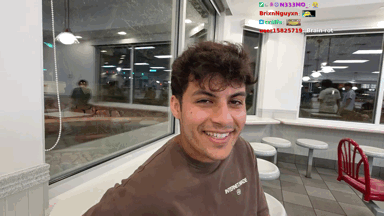 A Young Man Wearing A Brown Shirt That Says Principle Smiles In A Diner GIF