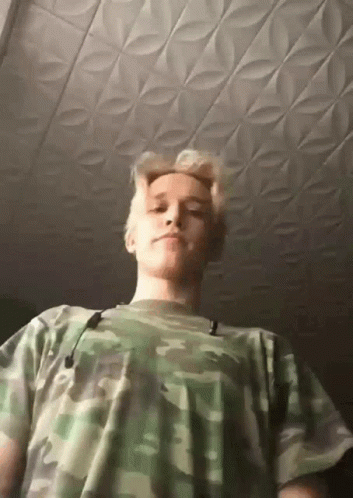 A Young Man Wearing A Camouflage Shirt Is Looking Down At The Camera GIF