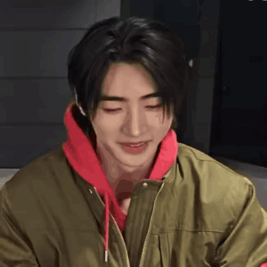 A Young Man Wearing A Green Jacket And A Red Hoodie Smiles GIF