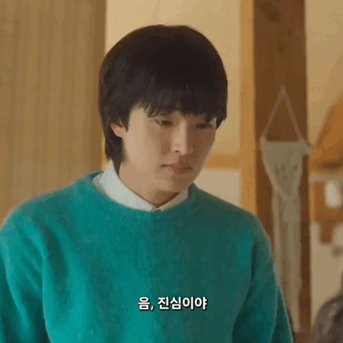 A Young Man Wearing A Green Sweater And A White Shirt Is Looking Down . GIF
