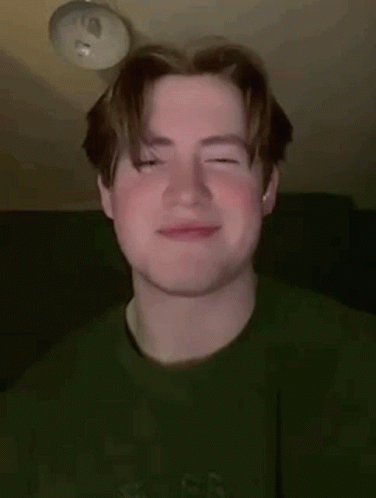 A Young Man Wearing A Green Sweater Is Smiling With His Eyes Closed . GIF