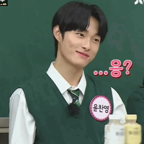 A Young Man Wearing A Green Vest And Tie Is Smiling While Standing In Front Of A Blackboard .. GIF