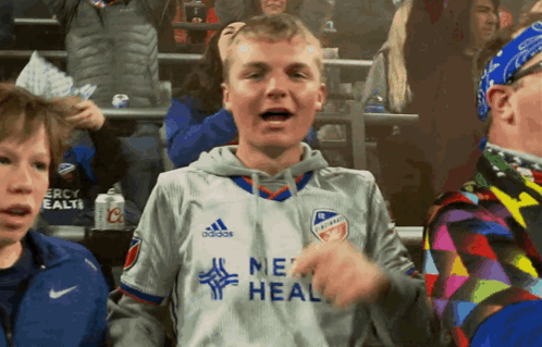 A Young Man Wearing A Grey Adidas Jersey Stands In A Crowd GIF