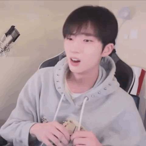 A Young Man Wearing A Grey Hoodie Is Sitting In Front Of A Microphone .. GIF