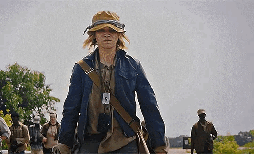 A Young Man Wearing A Hat And A Jacket Is Walking Down A Street . GIF