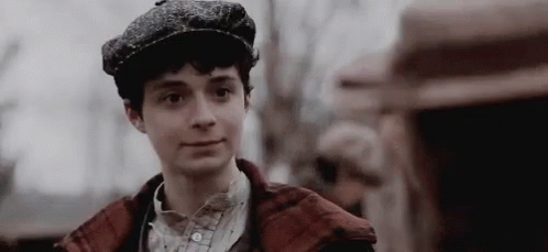 A Young Man Wearing A Hat And A Plaid Jacket Is Smiling . GIF