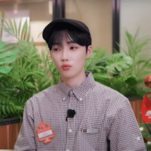 A Young Man Wearing A Hat And A Plaid Shirt Is Sitting In Front Of A Plant . GIF
