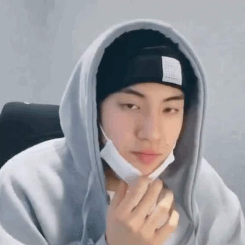A Young Man Wearing A Hoodie And A Beanie Is Holding His Hand To His Face . GIF