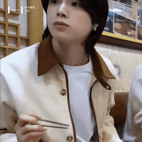 A Young Man Wearing A Jacket And A White Shirt Is Holding Chopsticks In His Hand . GIF