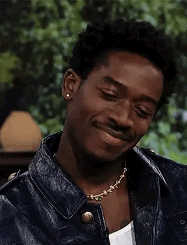 A Young Man Wearing A Leather Jacket And A Necklace Is Smiling . GIF