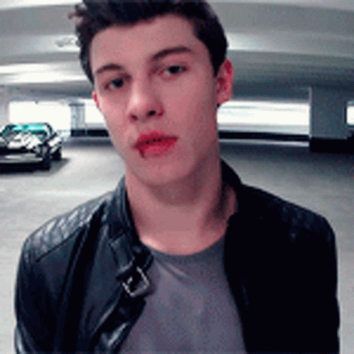 A Young Man Wearing A Leather Jacket Is Standing In A Parking Garage Looking At The Camera . GIF