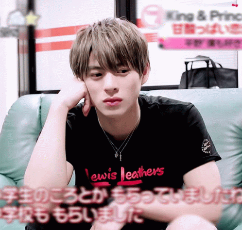 A Young Man Wearing A Lewis Leathers Shirt Sits On A Green Couch GIF