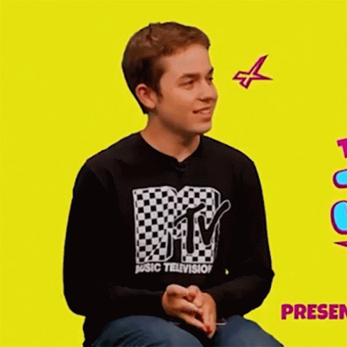 A Young Man Wearing A Mtv Music Television Shirt Is Sitting On A Yellow Background . GIF