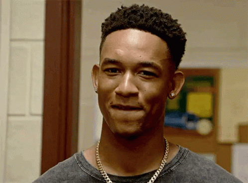 A Young Man Wearing A Necklace And Earrings Is Smiling . GIF