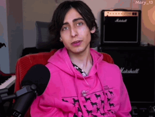 A Young Man Wearing A Pink Hoodie Is Sitting In Front Of A Marshall Amplifier GIF