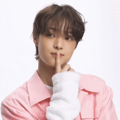 A Young Man Wearing A Pink Jacket Is Holding His Finger To His Mouth . GIF