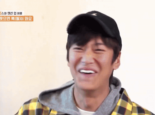 A Young Man Wearing A Plaid Shirt And A Black Hat Smiles GIF