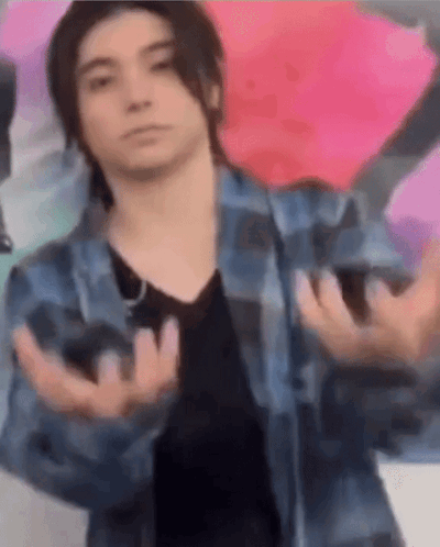 A Young Man Wearing A Plaid Shirt And A Black Shirt Is Making A Funny Face With His Hands Outstretched . GIF