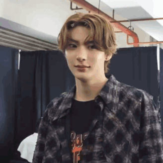 a young man wearing a plaid shirt and a black t-shirt is making a funny face .
