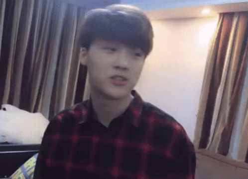 A Young Man Wearing A Plaid Shirt Is Sitting In A Room With Curtains . GIF