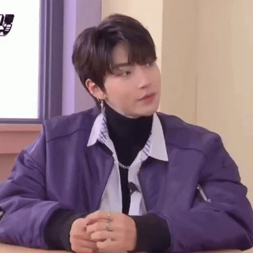 A Young Man Wearing A Purple Jacket And A Turtleneck Is Sitting At A Table . GIF