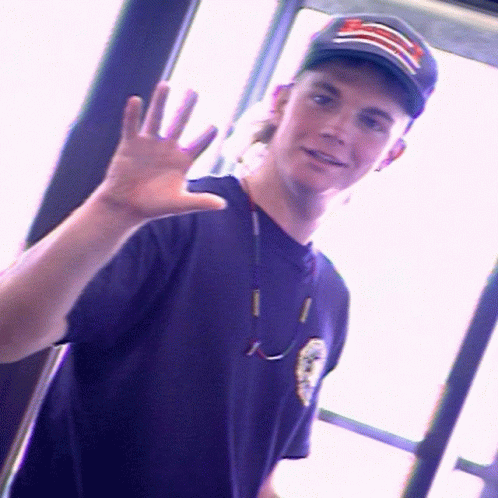 A Young Man Wearing A Purple Shirt And A Black Hat With A Red White And Blue Stripe On It GIF