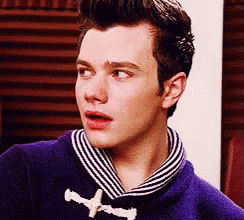 A Young Man Wearing A Purple Sweater And A Striped Scarf Looks At The Camera . GIF