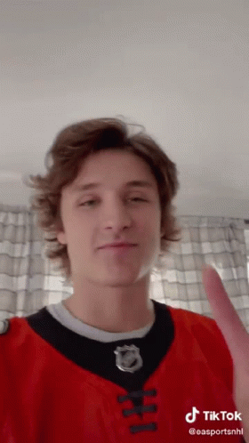 A Young Man Wearing A Red And Black Jersey With A Nhl Logo On It GIF
