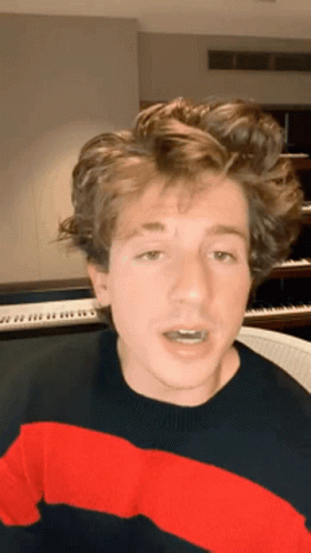 A Young Man Wearing A Red And Black Striped Sweater Is Sitting In Front Of A Piano Keyboard . GIF
