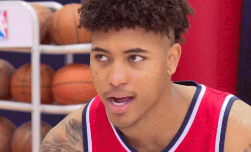 a young man wearing a red and white basketball jersey is standing in front of a basketball rack .
